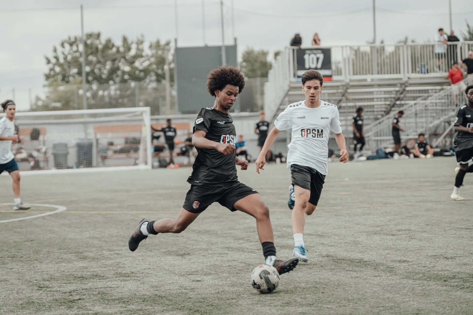 Player in black kit striking a pass under pressure